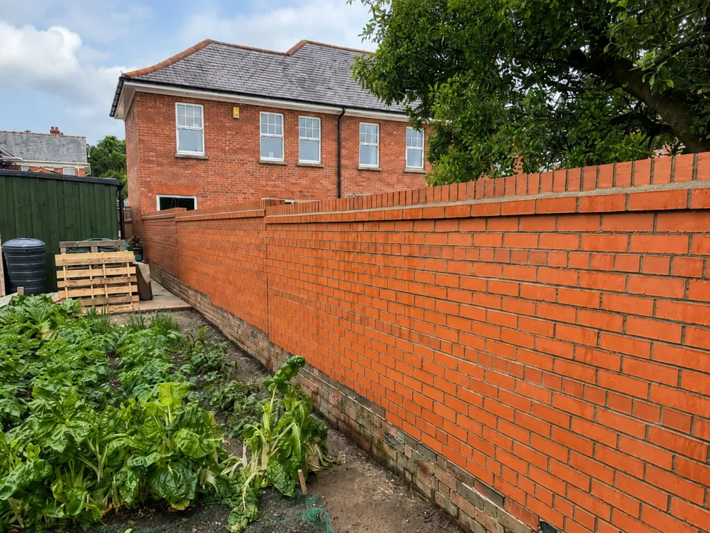 A long red brick boundary wall with a soldier course to the top, running alongside a planted bed.