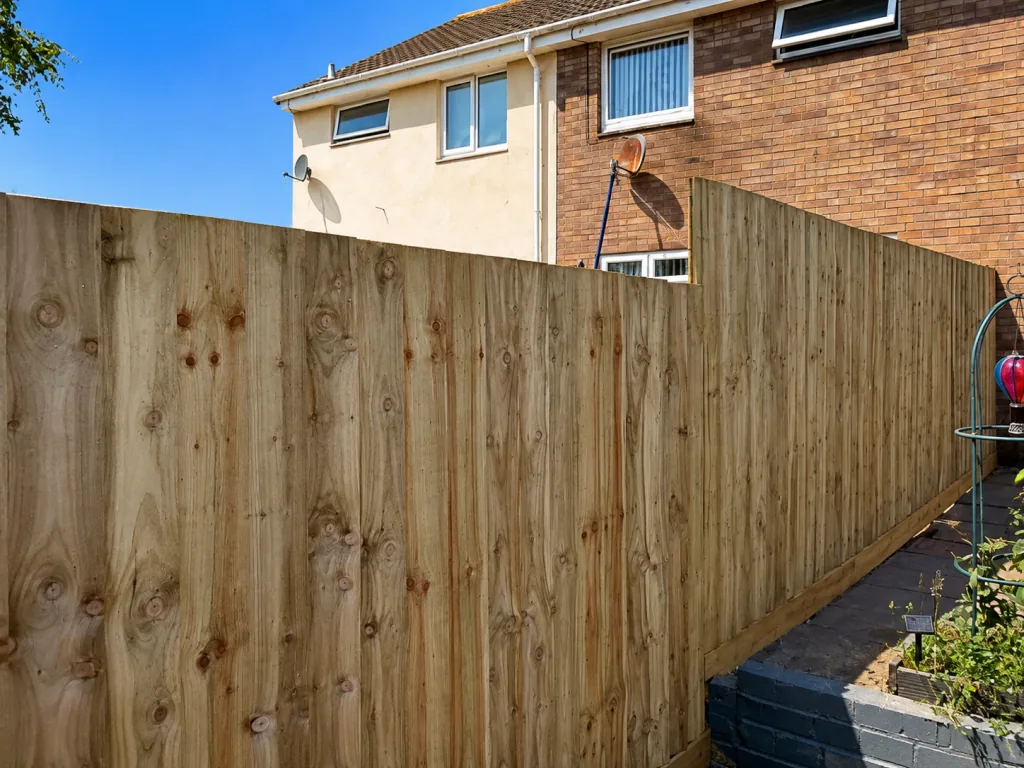 A run of new close-board timber fencing along a residential boundary, stepping down beside a paved path.