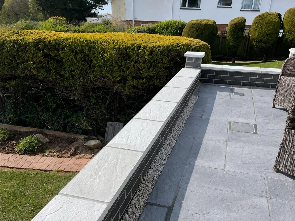 Grey paved terrace with a charcoal brick retaining wall, pale coping and a pebble drainage channel.
