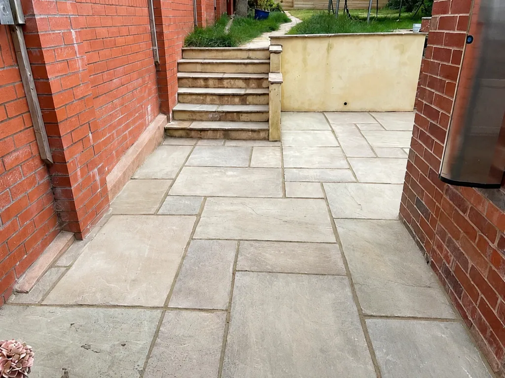 Sandstone paving laid between red brick walls, leading to a flight of stone steps rising to a garden.